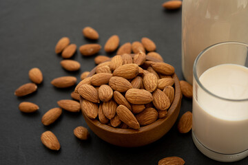 Almond milk with almond in a wooden bowl on black background. (selective focus; close-up shot)