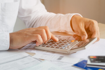 Close up hand of young asian businessman, male is pressing a calculator to calculate cost from invoice, bills or statement to plan his spending for payment, payday at home. Finance people concept.