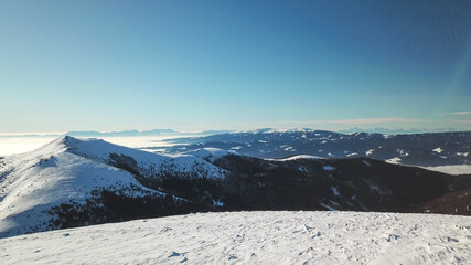 Obraz premium A drone shot of snow capped Alps in the region of Speikkogel in Austrian Alps. The whole are is covered with snow. Many mountain chains in the back. Thick fog in the valley. Winter outdoor activity.