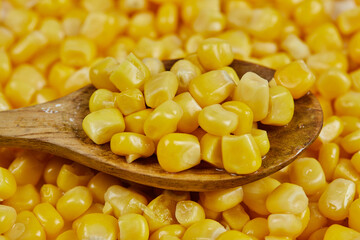 A heap of boiled sweet corn with a wooden spoon on a white table