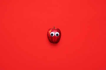 Red apple with googly eyes on a matching red background with copy space and room for text with a minimalistic composition