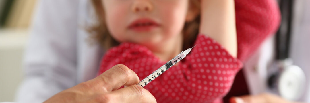 Cropped photo of male pediatrician making vaccination to small girl, while doctor holding a syringe. Medicine and care concept