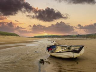 Aberffaw, Anglesey, Wales.  A small boat moored on the beach at Aberffraw with the sun setting.