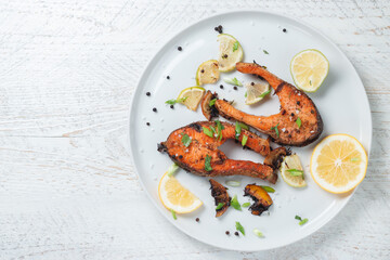 Grilled salmon steak with lemon, spices and lime in a white plate on a light wooden table. Deliciously cooked salmon fillet.