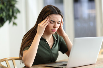 Stressed woman suffering migraine with a laptop at home