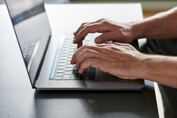 side view of a man's hands typing with his laptop on a wooden table
