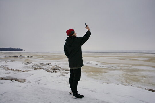 young man in full growth takes pictures on a smartphone in winter