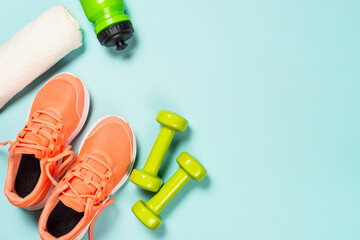 Fitness equipment. Sneakers, dumbbell, towel and bottle of water. Trayning, workout and fitness concept. Flat lay image on blue background with copy space.