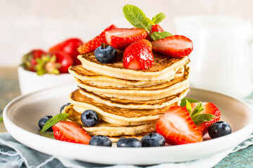 Pancakes with fresh berries and honey at kitchen table. Healthy breakfast or dessert.