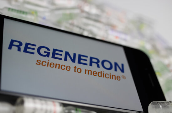 Viersen, Germany - May 9. 2020: Close up of mobile phone screen with logo lettering of Regeneron pharmaceutical company on pile drug ampules (selective focus on letter t in center)
