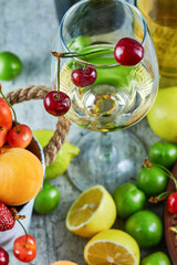 Bucket of summer fruits, lemon and a glass of white wine on marble background