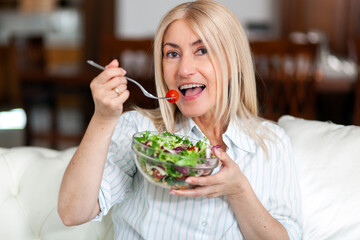 Mature woman eating a healthy salad on her sofa