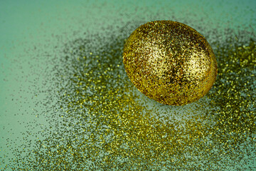 Trendy easter background with shiny golden colored egg and with glitters around. Creative spring holiday image with painted chicken egg. Top view flat lay still life. Easter concept.