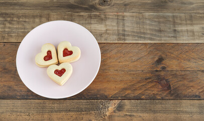 Dish with three heart-shaped cookies on a wooden base. Copy space.