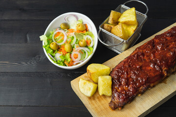 Ribs in barbecue sauce with salad and potatoes on a black background.