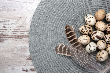 Quail eggs and feathers on grey round placemat. Copy space