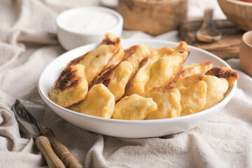 Baked dumplings (pierogi) with cottage cheese stuffing in a ceramic bowl on a wooden table, close-up. Vegetarian dish