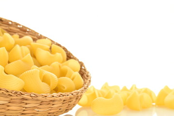 Bright yellow uncooked pasta in a straw dish, close-up, isolated on white.