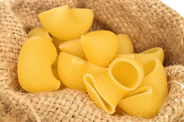 Bright yellow uncooked pasta in a jute bag, close-up.