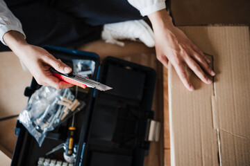 close up of young woman assembling furniture at home working with cutter. DIY concept