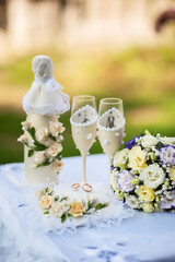 Bride's and groom's wedding wineglasses, bottle of champagne and bridal bouquet decorated with white flowers on ceremony table. Summer garden wedding ceremony outdoor with green grass background.