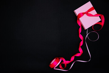 On a black background, there is a pink gift box. The box is tied with a satin ribbon.Gift wrapping.