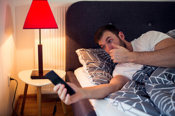 Young man uses his smartphone in bed before sleep