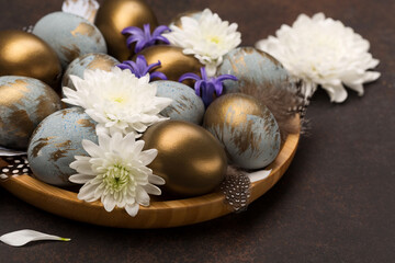 Easter Decoration with gray blue golden eggs, quail feathers, white flowers on dark wooden background. Selective focus, copy space.