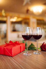 Romantic dinner. Two glasses of wine, red rose red gift box on wooden table.  Valentine's Day, holiday and surprise concept.