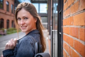 A beautiful, young and stylish woman poses in front of a camera near a brick wall. A large portrait