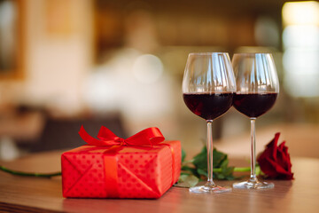 Romantic dinner. Two glasses of wine, red rose red gift box on wooden table.  Valentine's Day, holiday and surprise concept.