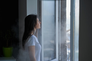 Fototapeta na wymiar Cold winter weather. Woman step to window, open it and frosty air rushes from outside through open windows to apartment. Airing housing in cold winter