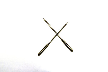 Sewing machine needles cross each other on white.