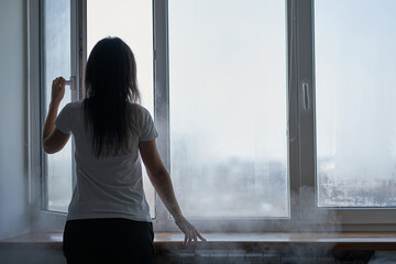 Cold winter weather. Woman step to window, open it and frosty air rushes from outside through open...