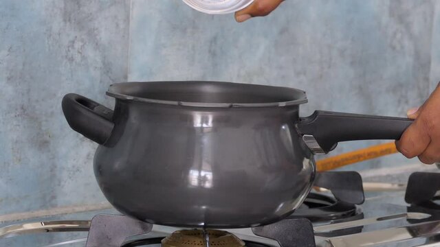Close shot of a black pressure cooker, hand pouring rice in it