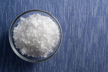 Glass bowl of sea salt on white and blue background with empty space