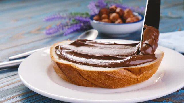 Spreading hazelnut cream on white bread slice, chocolate nut butter on school lunch toast