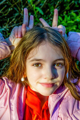 teenage girl with long hair holds horn-shaped fingers above her head under sunlight