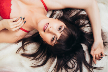 Naklejka premium Sexy brunette in red lingerie lies on the white carpet and smiles