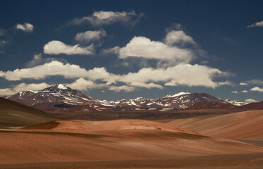 Enchanting alpine landscape. View of the desert dunes, sand and Andes mountain range under a magical blue sky with clouds. 