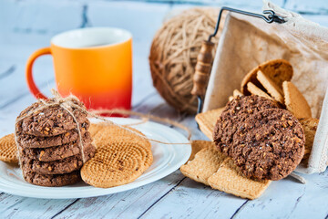 Assorted biscuits in plate and basket and a cup on blue table