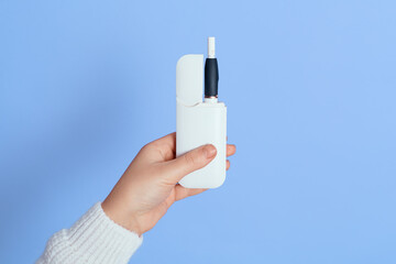 Close up portrait of faceless woman holding e-cigarette in hand, unknown female wearing while shirt posing with electronic ciggy isolated over blue background.