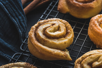 Closeup of a homemade cinnamon roll on a cooling rack on dark blue background.