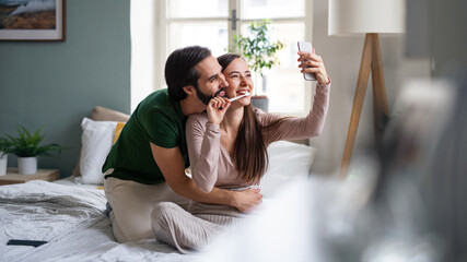 Young couple taking selfie on bed indoors at home.