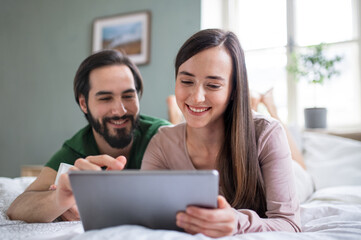 Young couple in love using tablet on bed indoors at home.