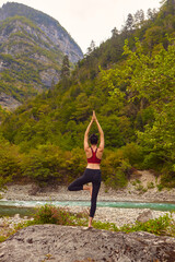 Yoga classes in nature. The concept of playing sports alone. Social exclusion. A woman does yoga on rocks, near a mountain river flows