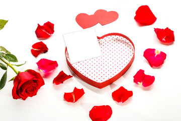 Postcard copy place in a box in the shape of a heart on a white background with a postcard in the middle of rose petals and red hearts next to a rose.