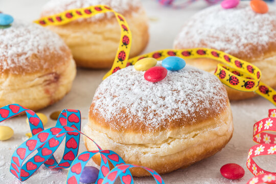 Krapfen, Berliner or donut with streamers, confetti and chocolate beans on white background. Colorful carnival or birthday image.