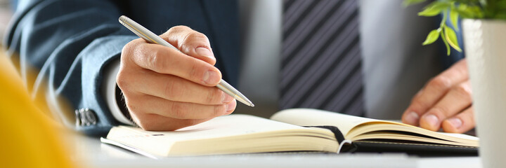 Cropped photo of busy man sitting at workplace in the office while making notes in notebook