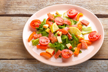Salad with salmon and cherry tomatoes and green salad in a plate on a wooden table.